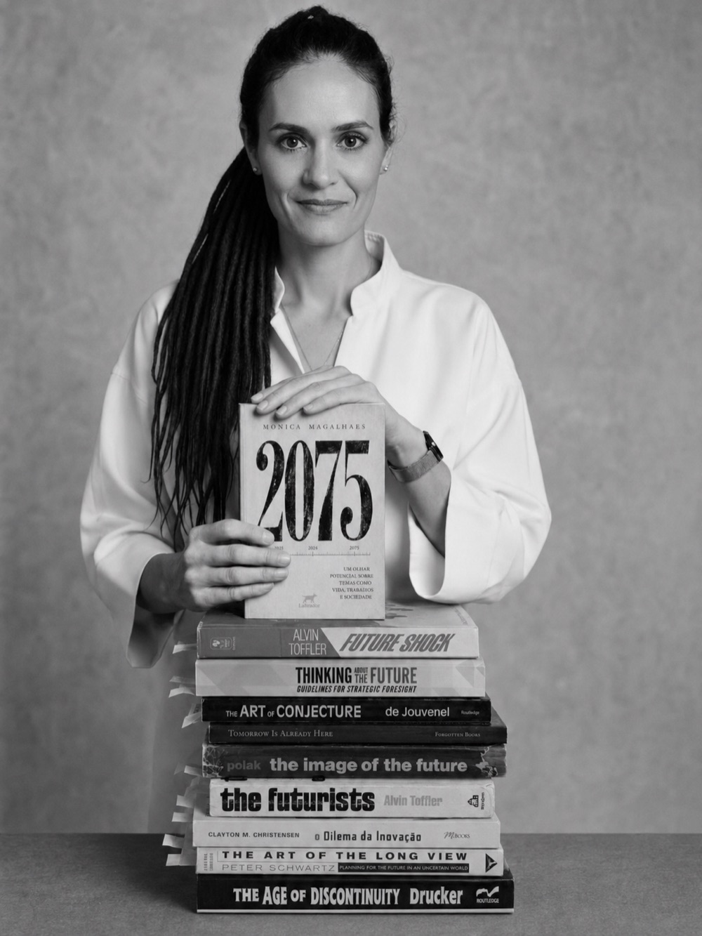 Monica Magalhaes com o livro 2075 sobre uma pilha de clássicos do futurismo